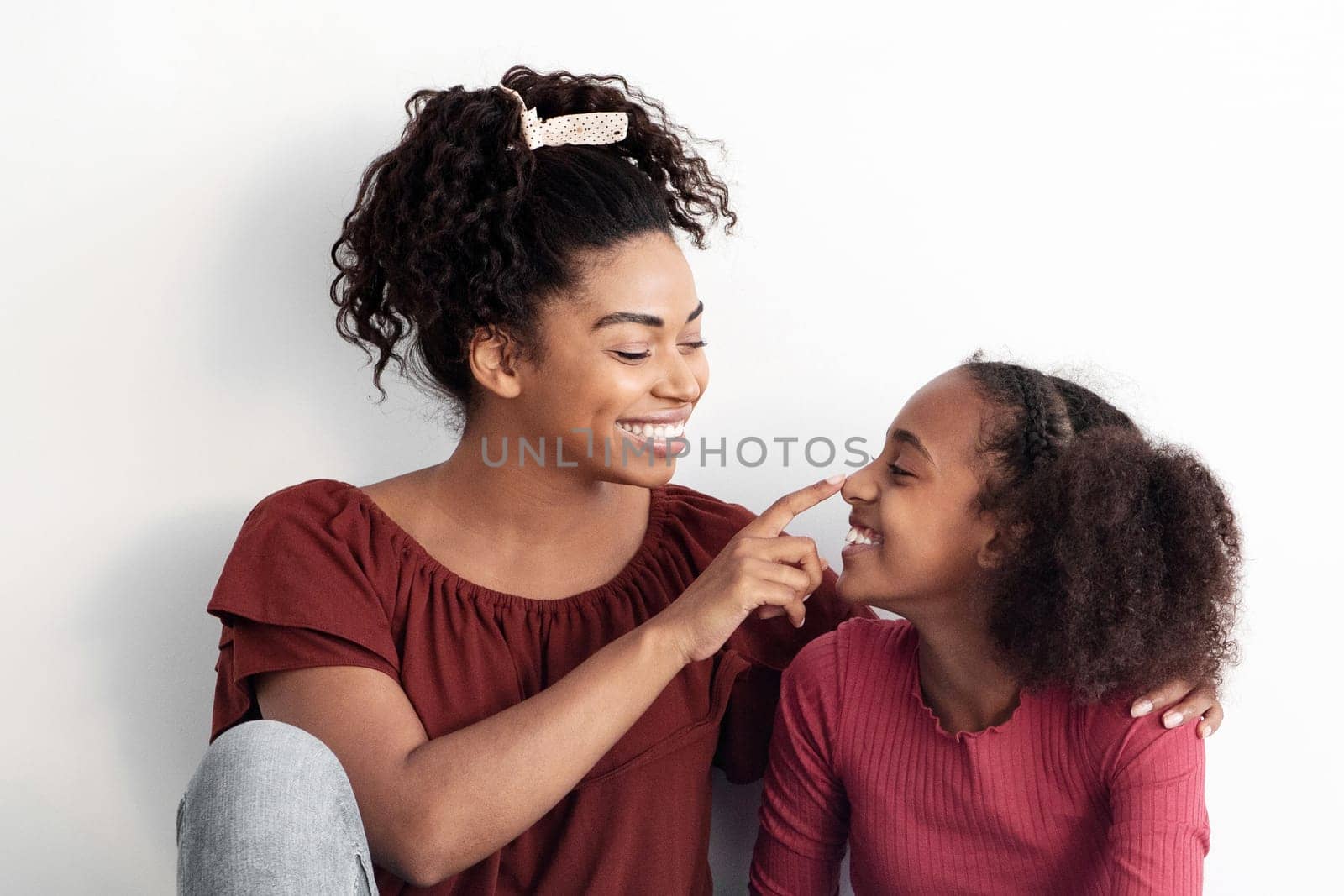Loving african american mother spending time with her cute daughter, young black woman and teen girl sitting on floor next to empty white wall together, bonding, laughing, copy space