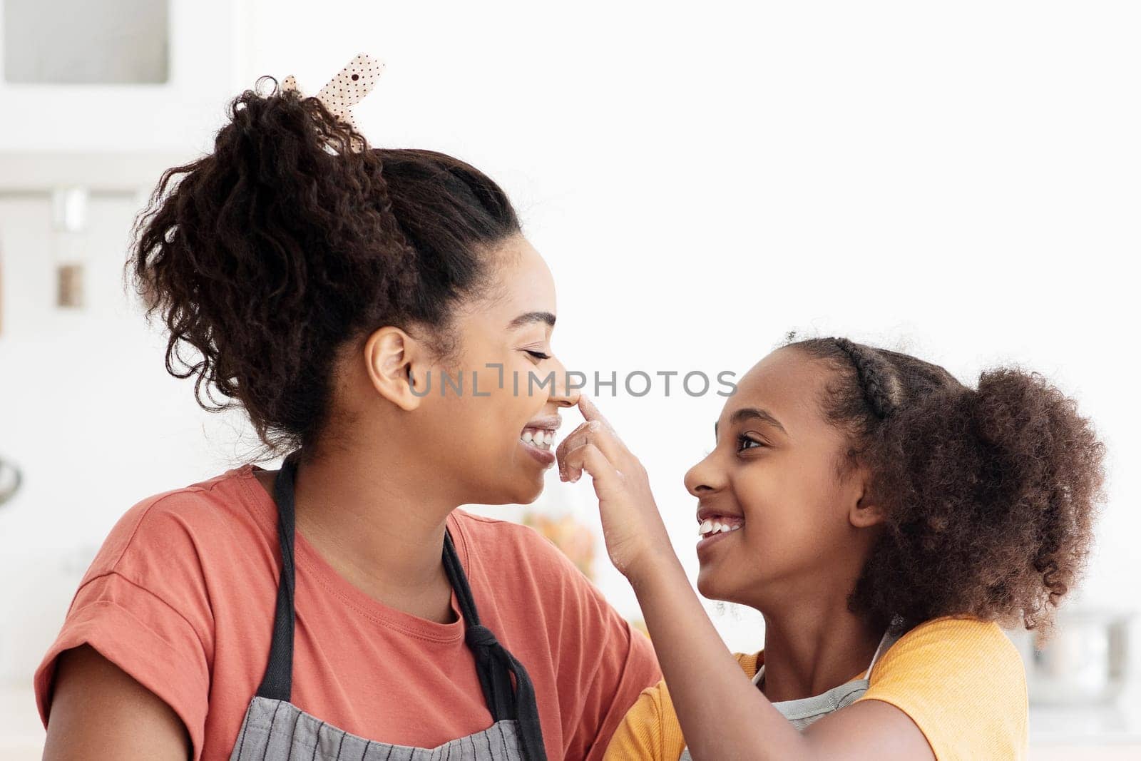 Happy afro-american mother and teen daughter in aprons having fun while baking, cheerful black mom and kid playing with flour while making dough for cookies at kitchen, enjoying time together