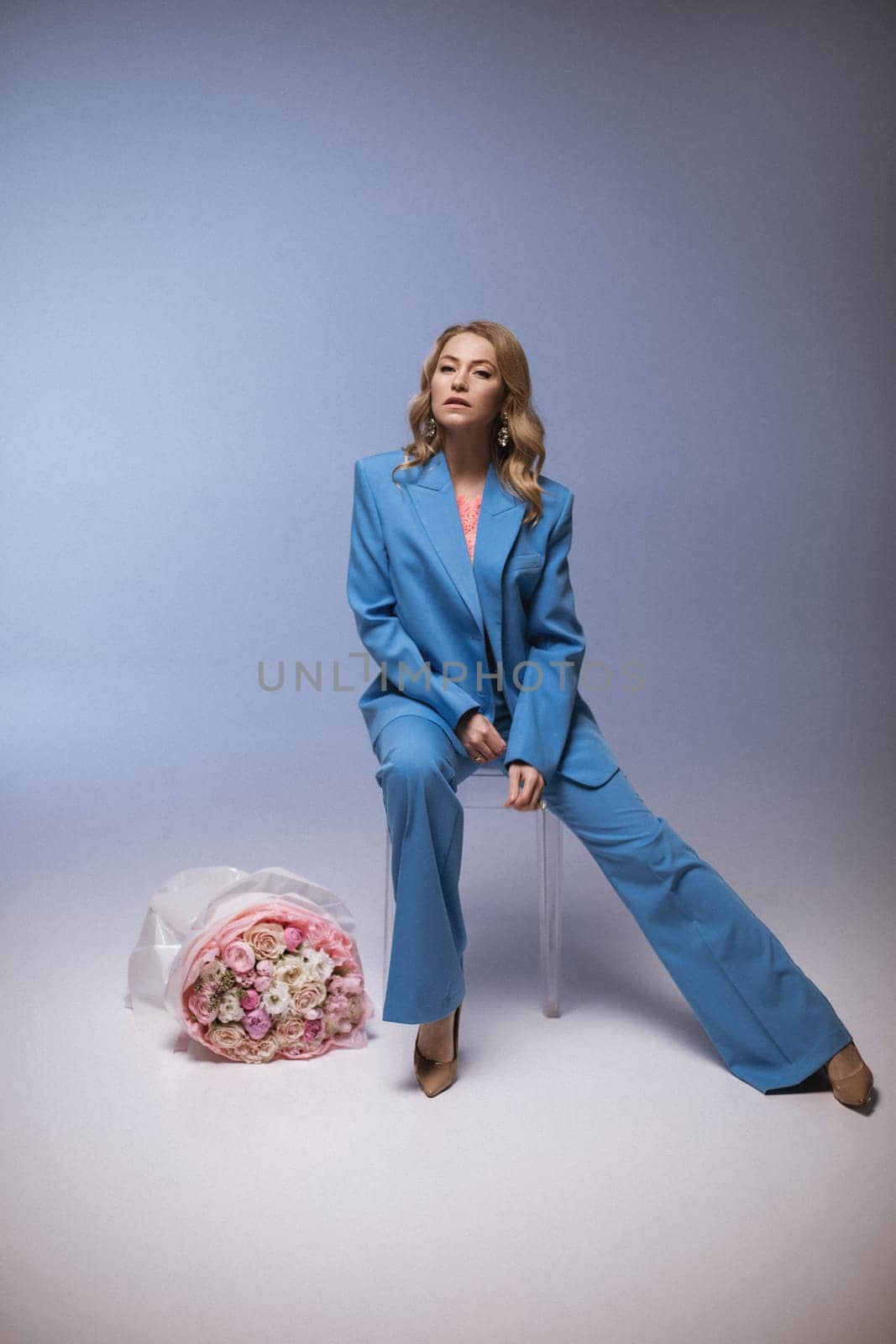Beautiful girl fashion model with soft pink makeup poses in an elegant blue pantsuit. Fashion and beauty.