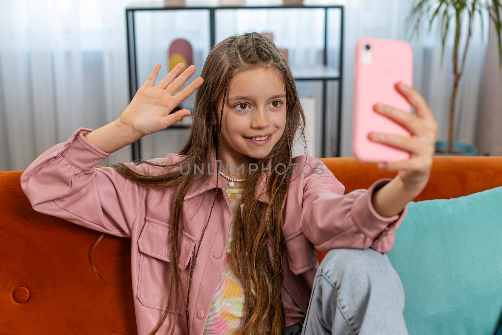 Happy young girl blogger taking selfie on smartphone, communicating video call online with social media subscribers. Female teenager child kid recording video story at home in living room on sofa.
