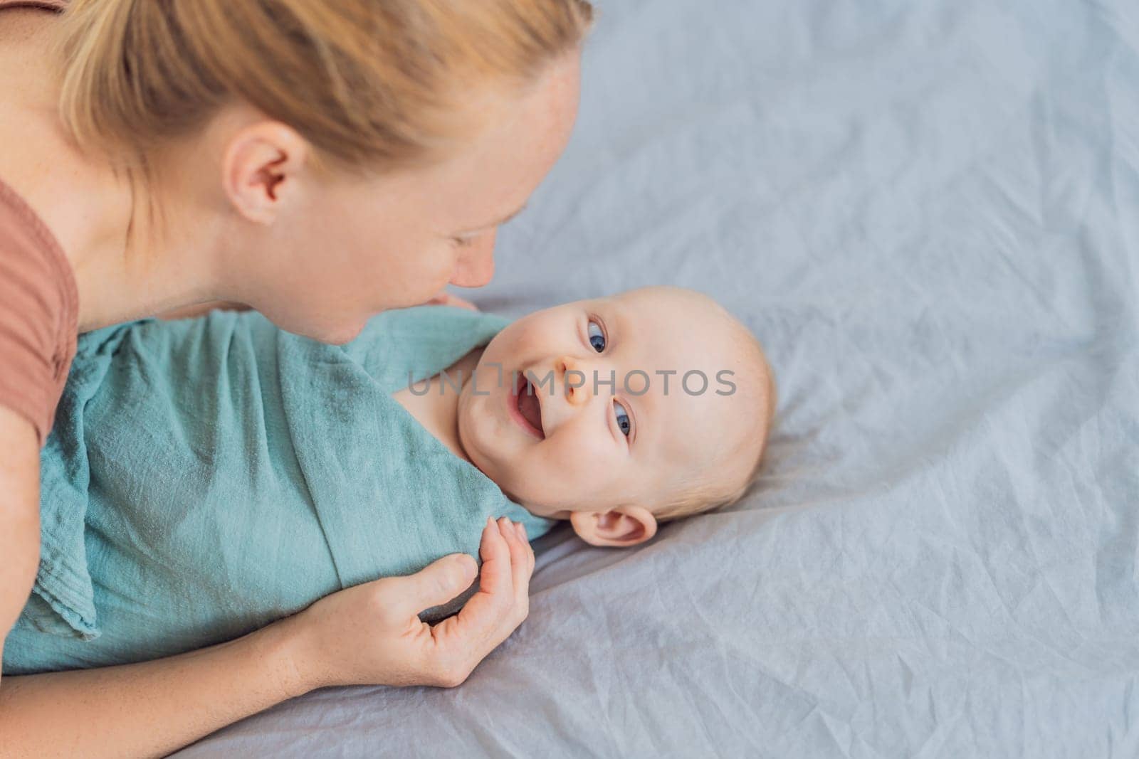 A mother gently wraps her baby in a soft muslin swaddle, providing warmth and comfort. A tender moment of care and love between mother and child. Motherhood, baby care, and nurturing concept