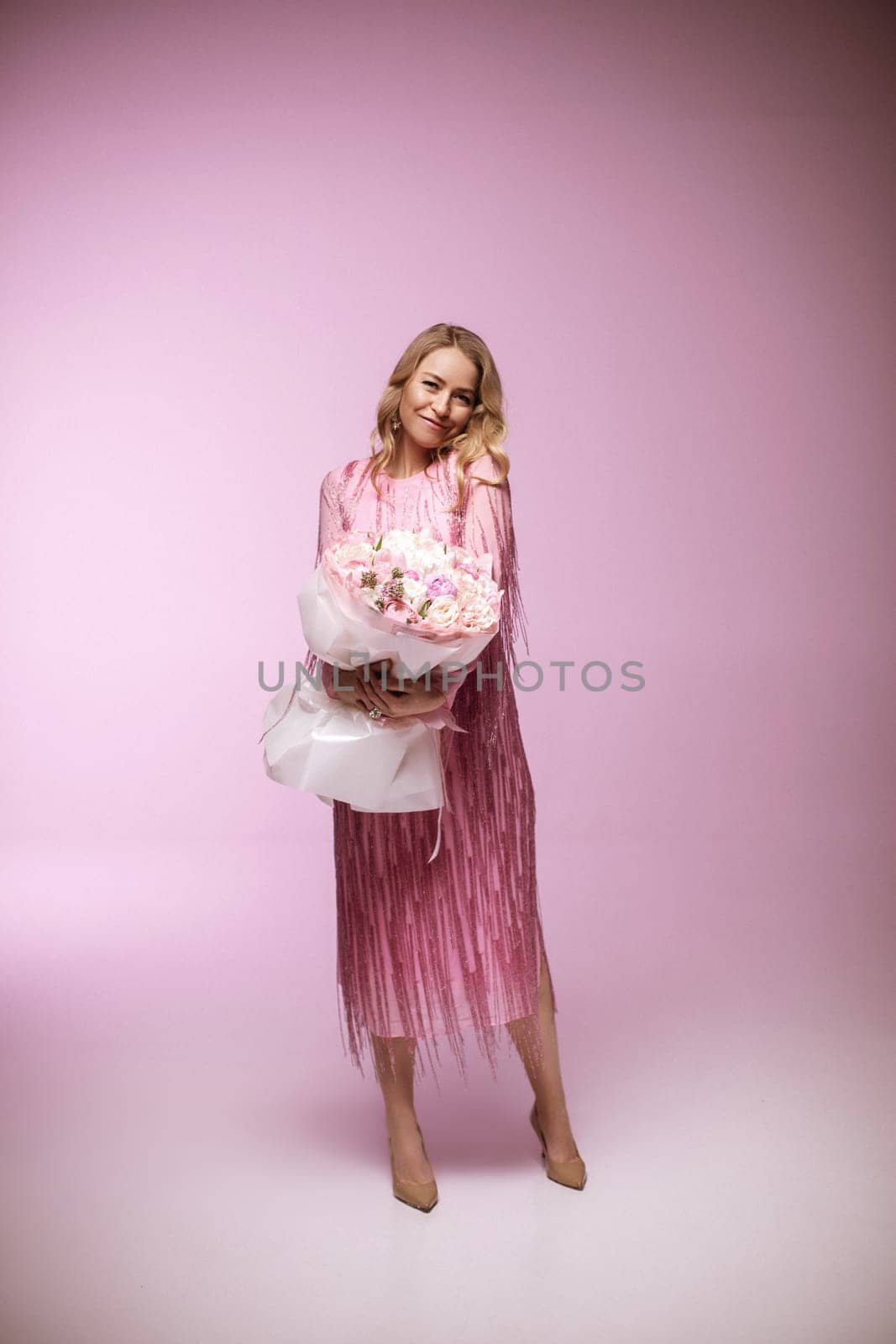 blonde hair poses with flower e, wearing a pink dress. Pink background.