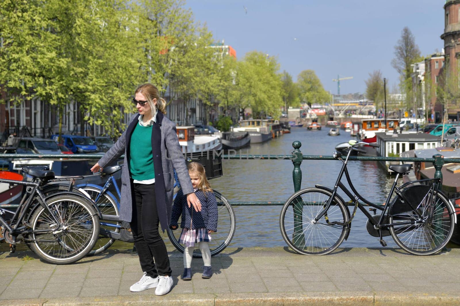 Blonde Dutchwoman mother with her daughter near the bicycle on the bridge over the water channel in Amsterdam city