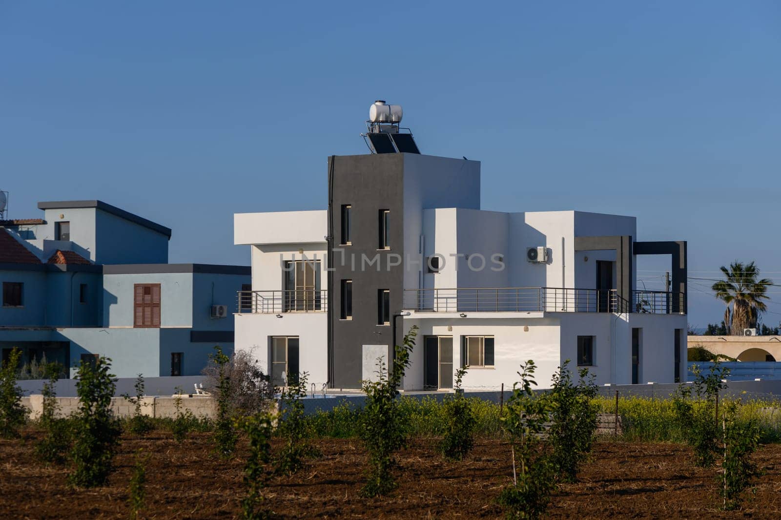 A beautifully designed house showcases sleek lines and contrasts with greenery under the vibrant sky in Cyprus.