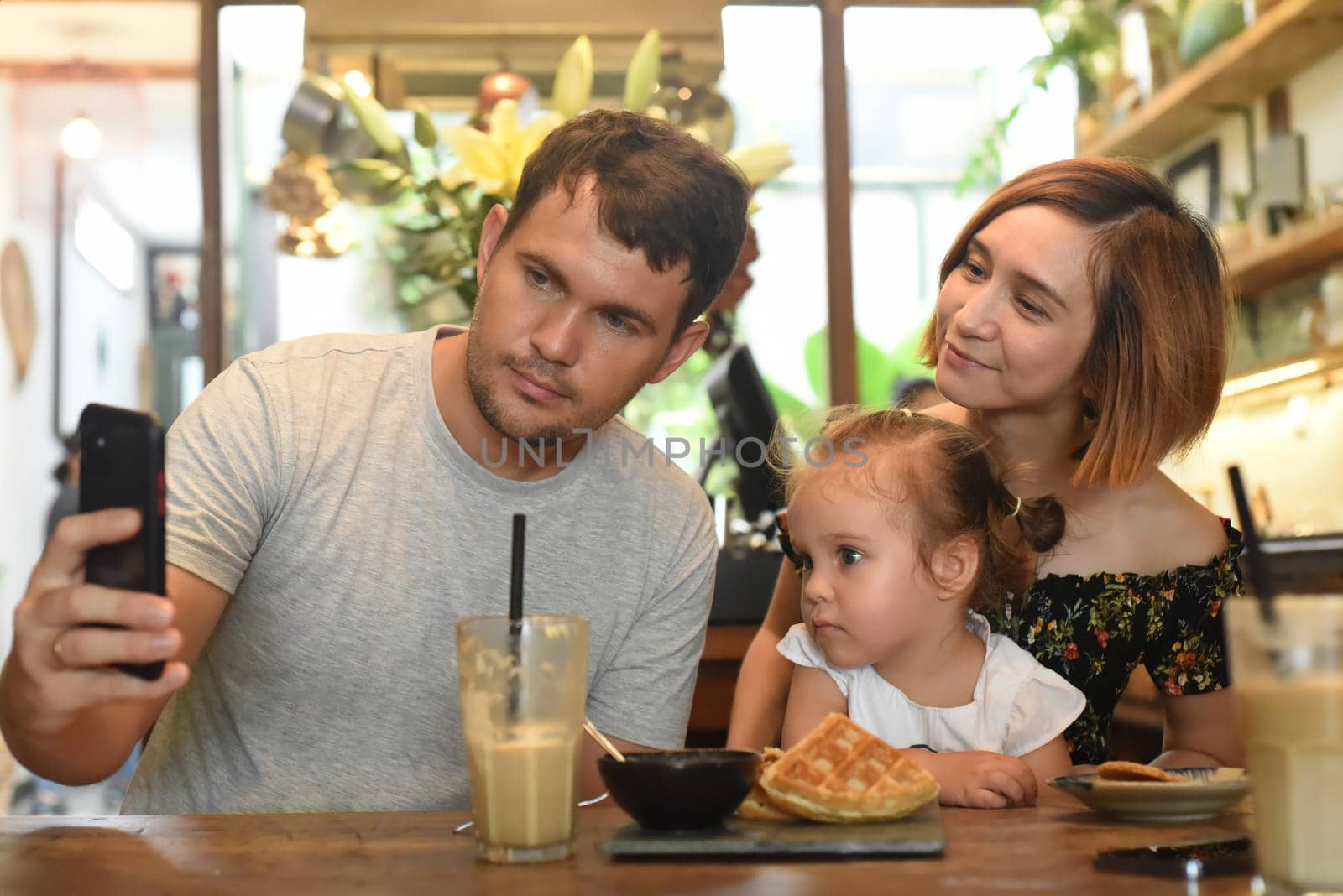 Young parents with daughter make selfie in a cafe