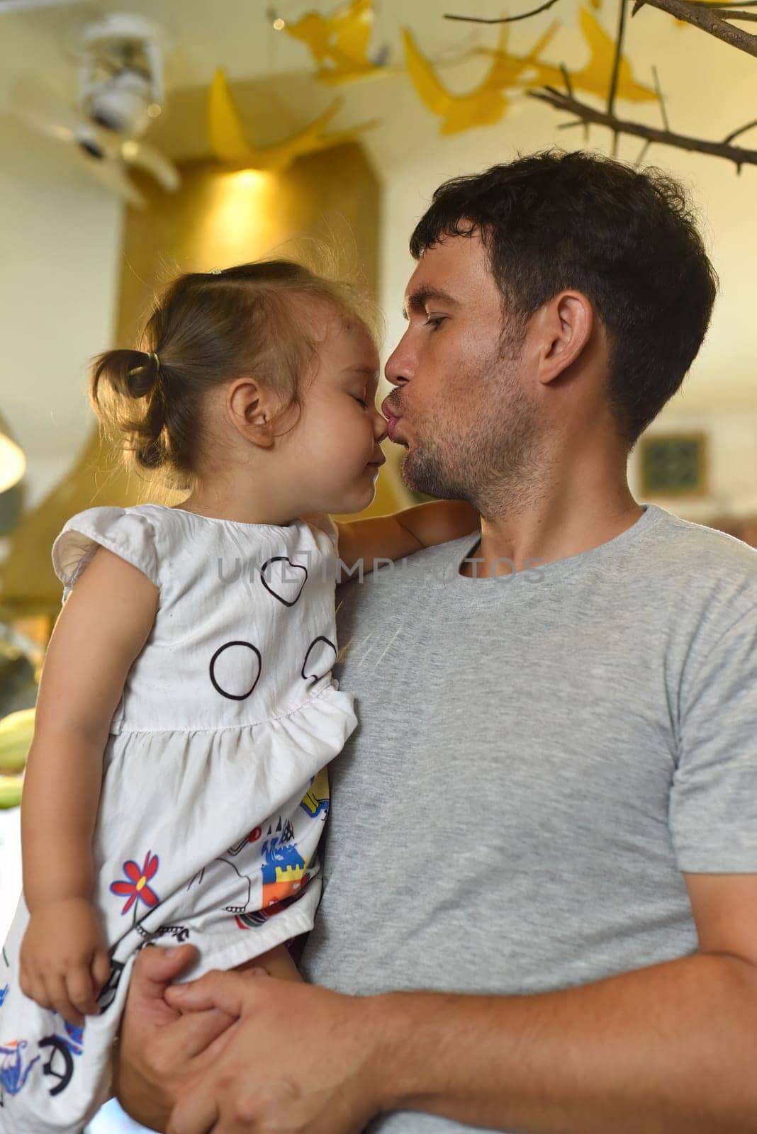 Young father kissing his daughter and holding her at his hands