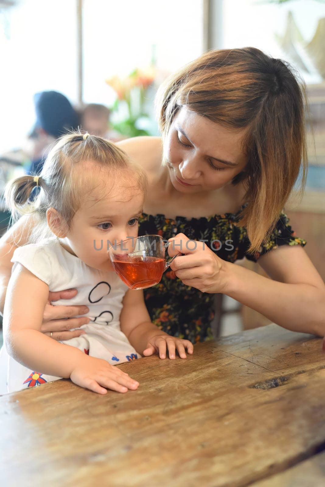 Young woman with a baby girl drinking tea from a tea pot in a coffee shop