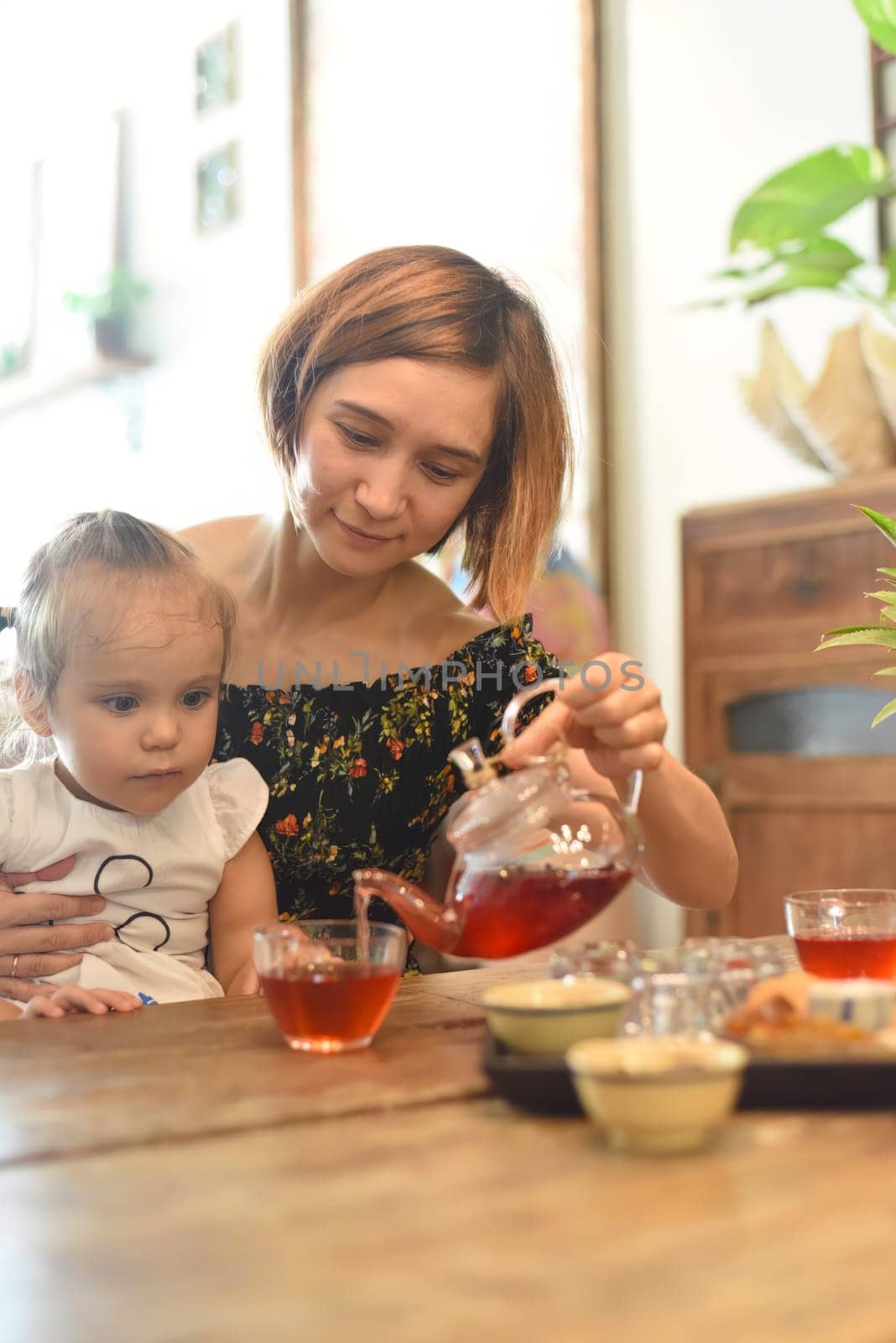 Young woman with a baby girl drinking tea from a tea pot in a coffee shop