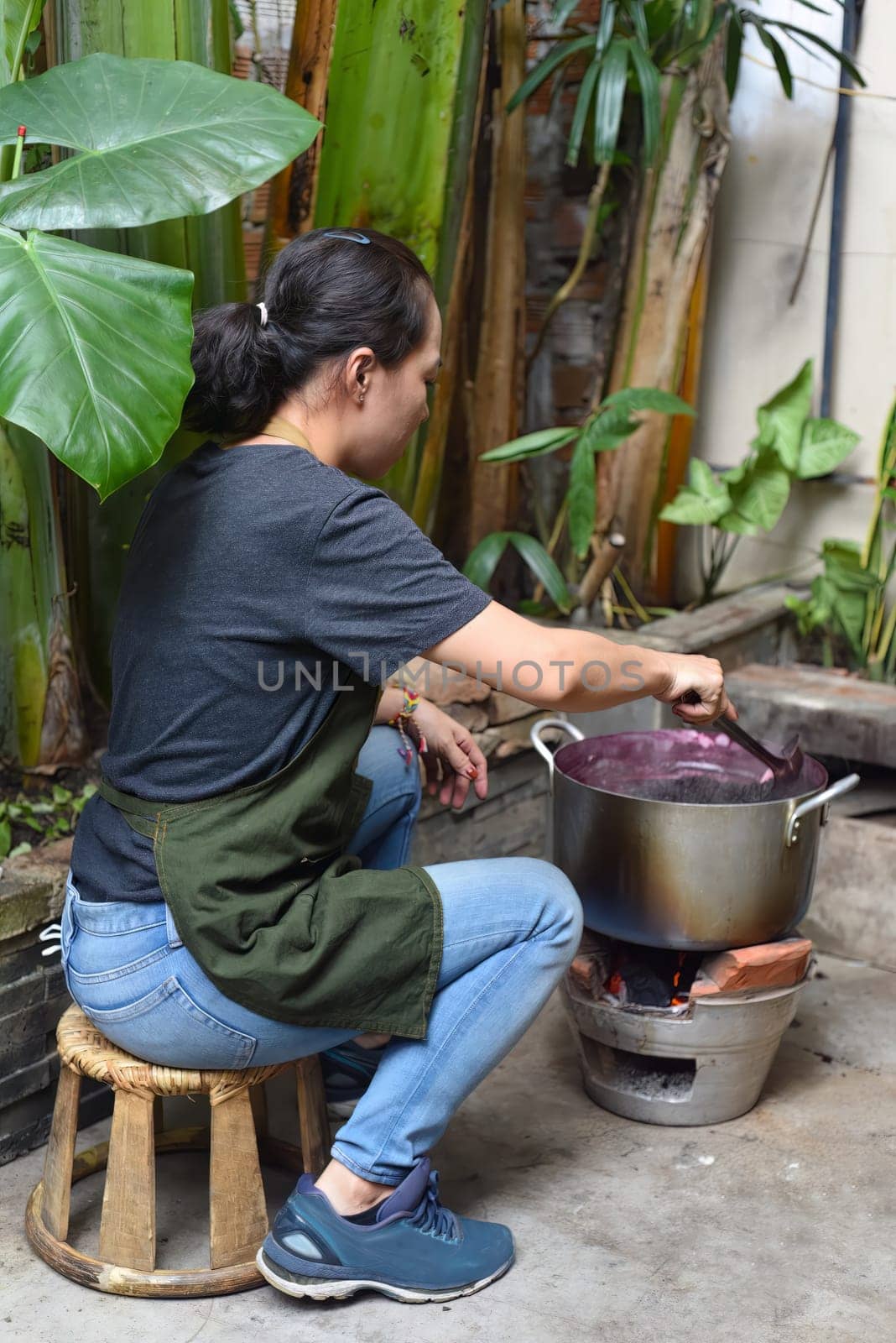 Young Vietnamese woman cooking a mulberry jam in a big saucepan