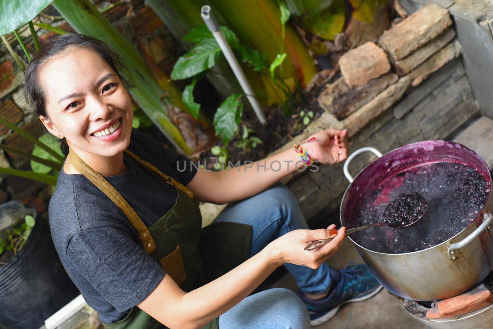 Young Vietnamese woman cooking a mulberry jam in a big saucepan