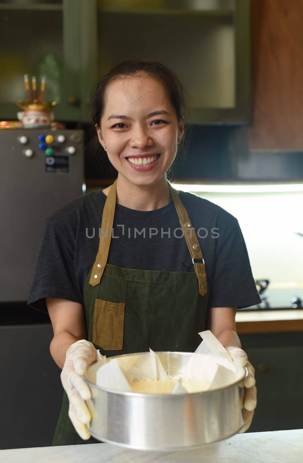 Vietnamese woman holding a baking dish with cheesecake dough in the kitchen