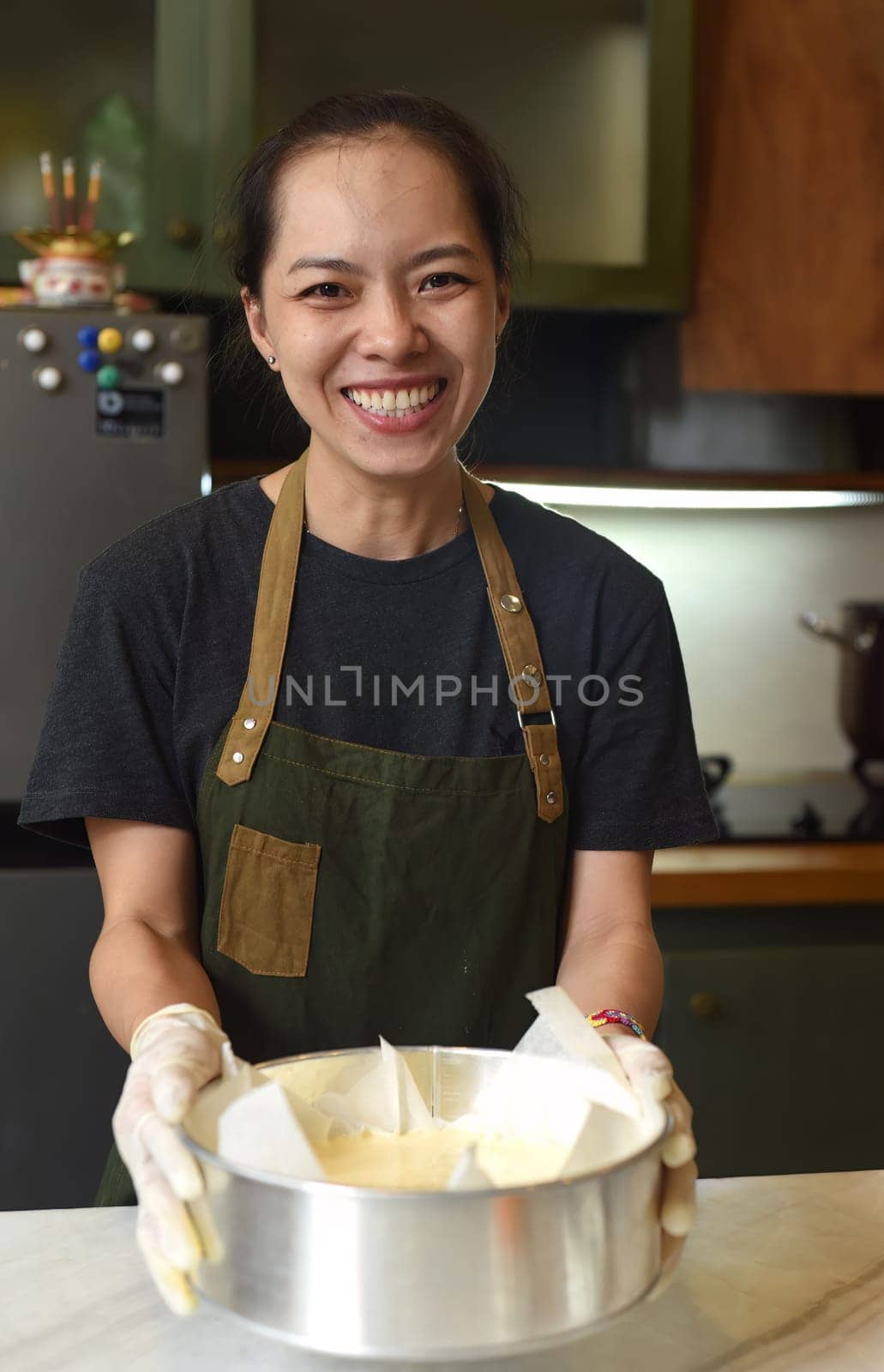 Vietnamese woman holding a baking dish with cheesecake dough in the kitchen
