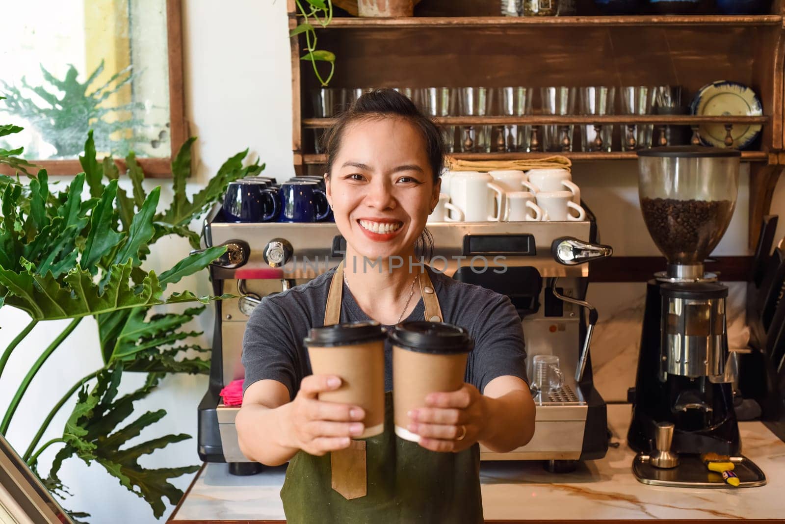 Vietnamese smiling waitress holding paper cups with coffee in a cafe