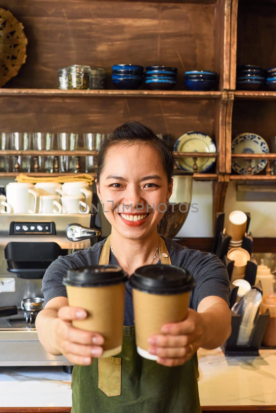 Vietnamese smiling waitress holding paper cups with coffee in a cafe