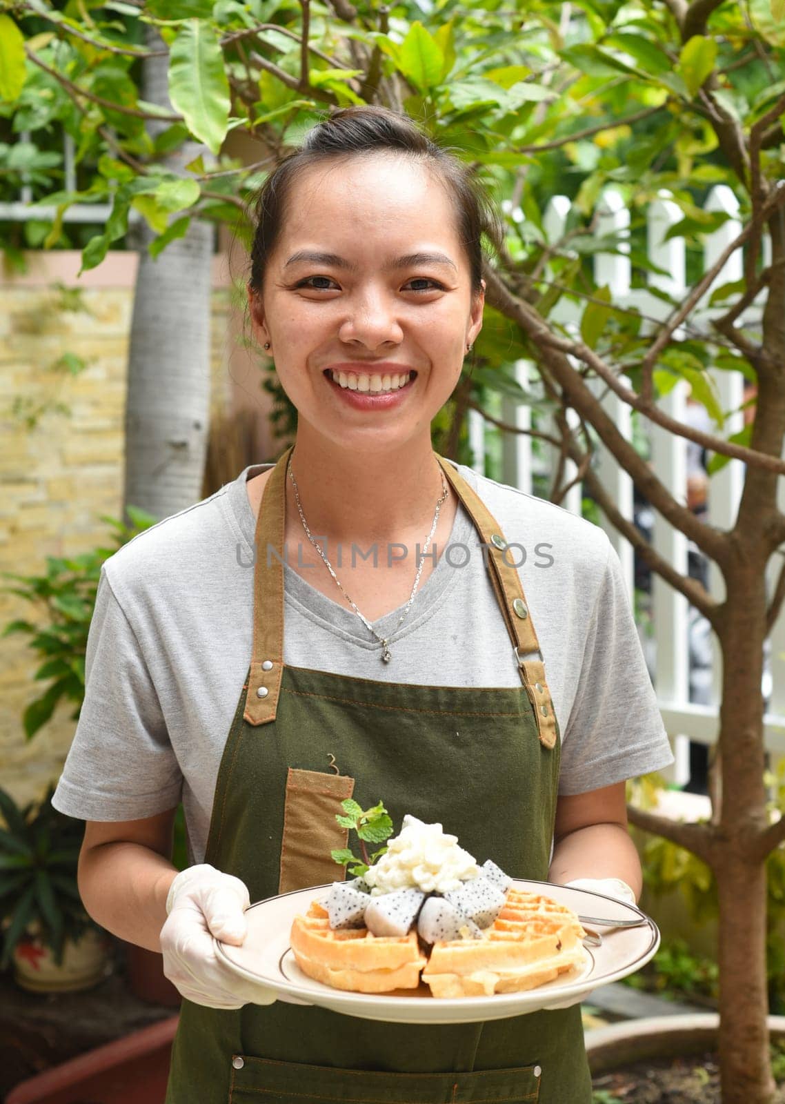 Vietnamese woman waitress serving Belgian waffles with fruits and ice cream in outdoor cafe