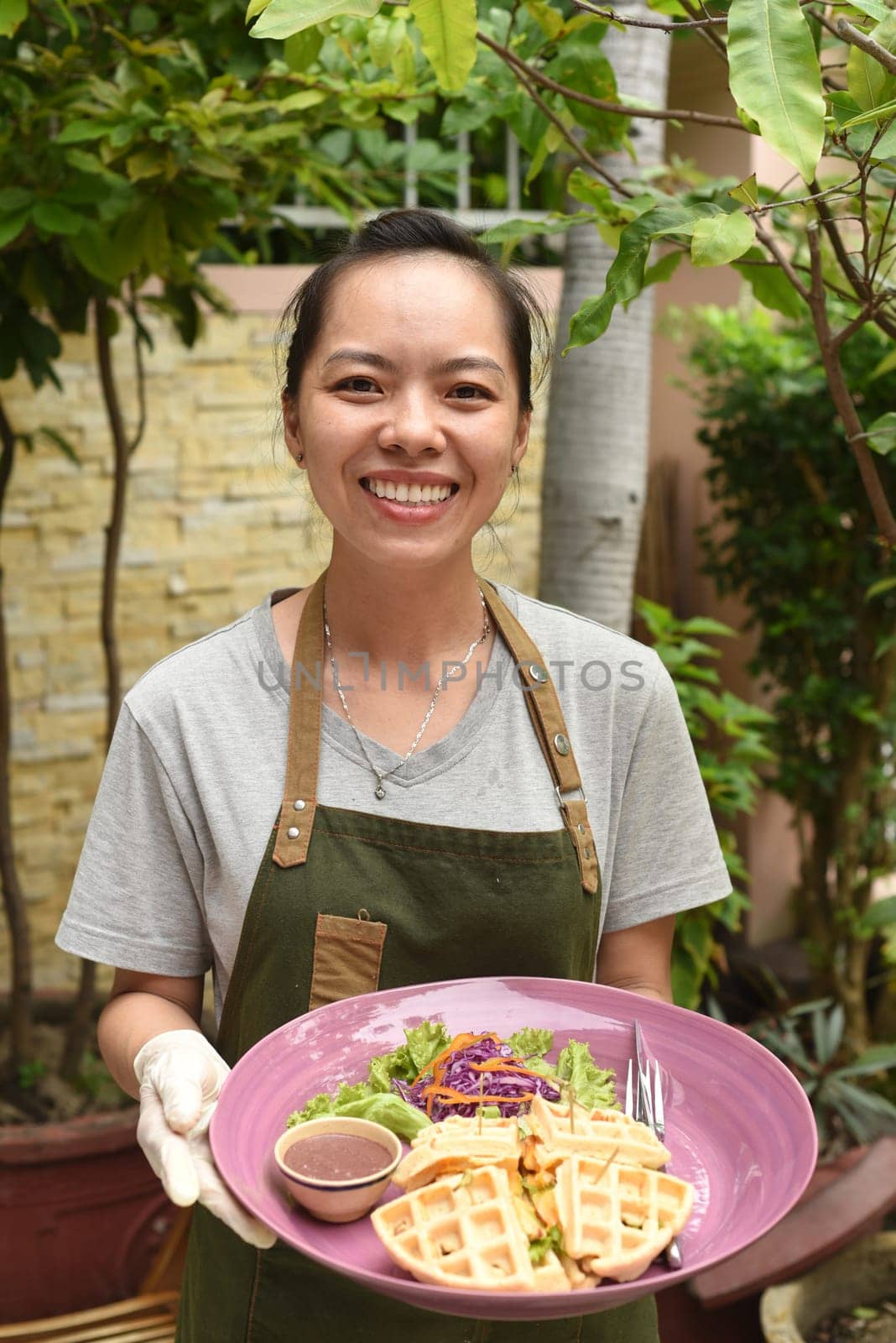 Vietnamese woman waitress serving Belgian waffles with greens and chicken in outdoor cafe