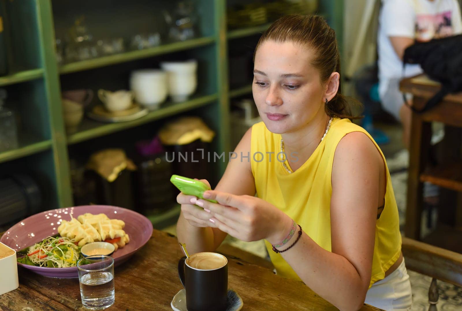 One caucasian woman scrolling a phone and preparing to eat her breakfast in cafe