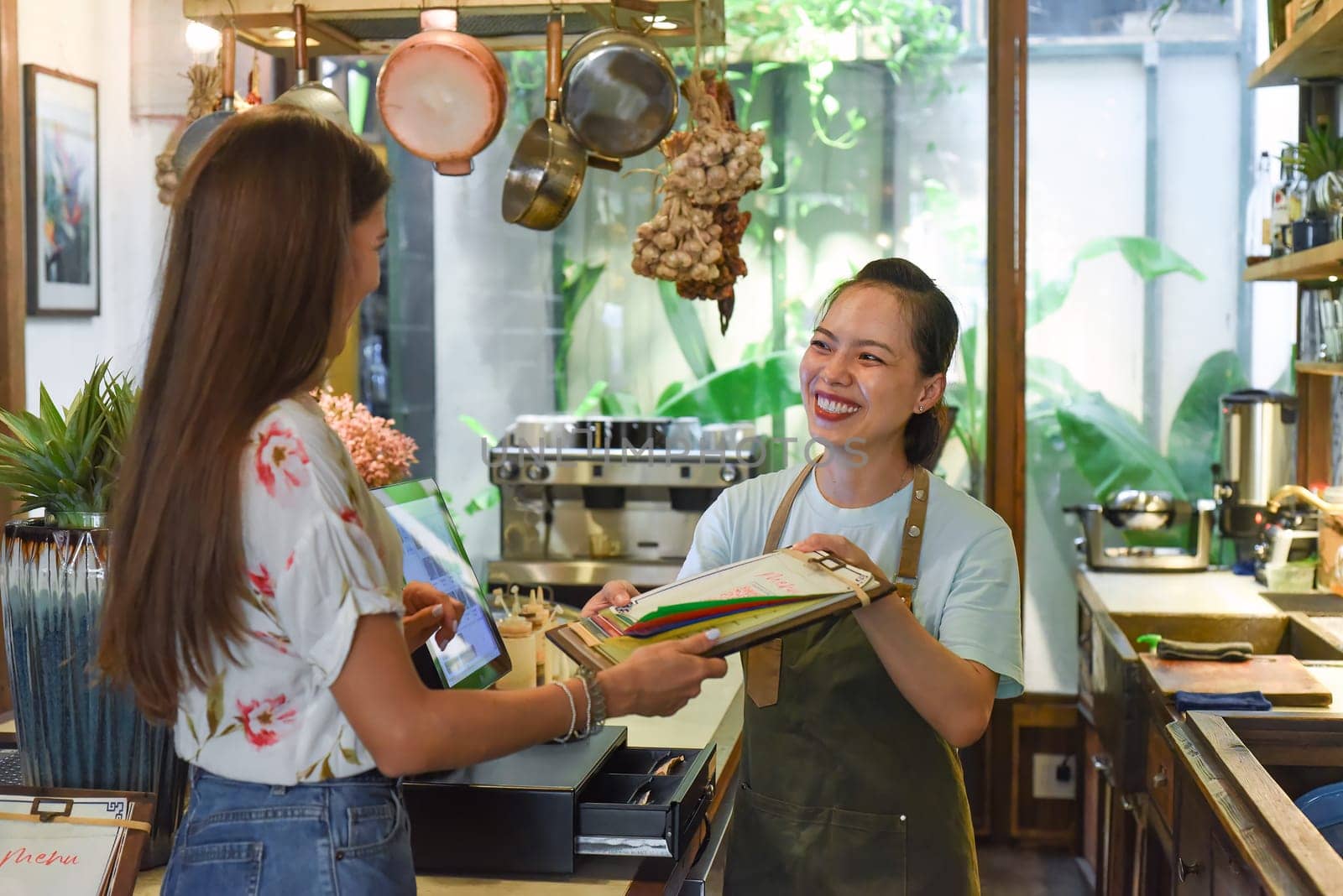 Young Vietnamese waitress working with check out machine and customers in cafe