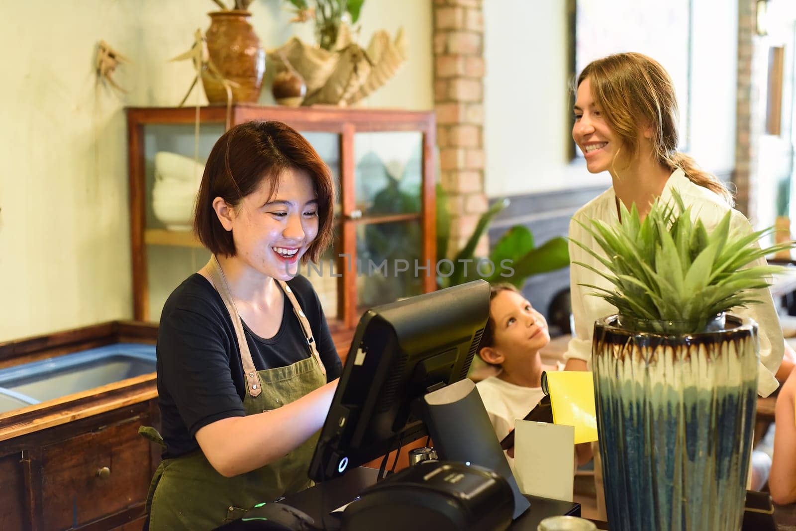Young Vietnamese waitress working with check out machine and with customers in cafe