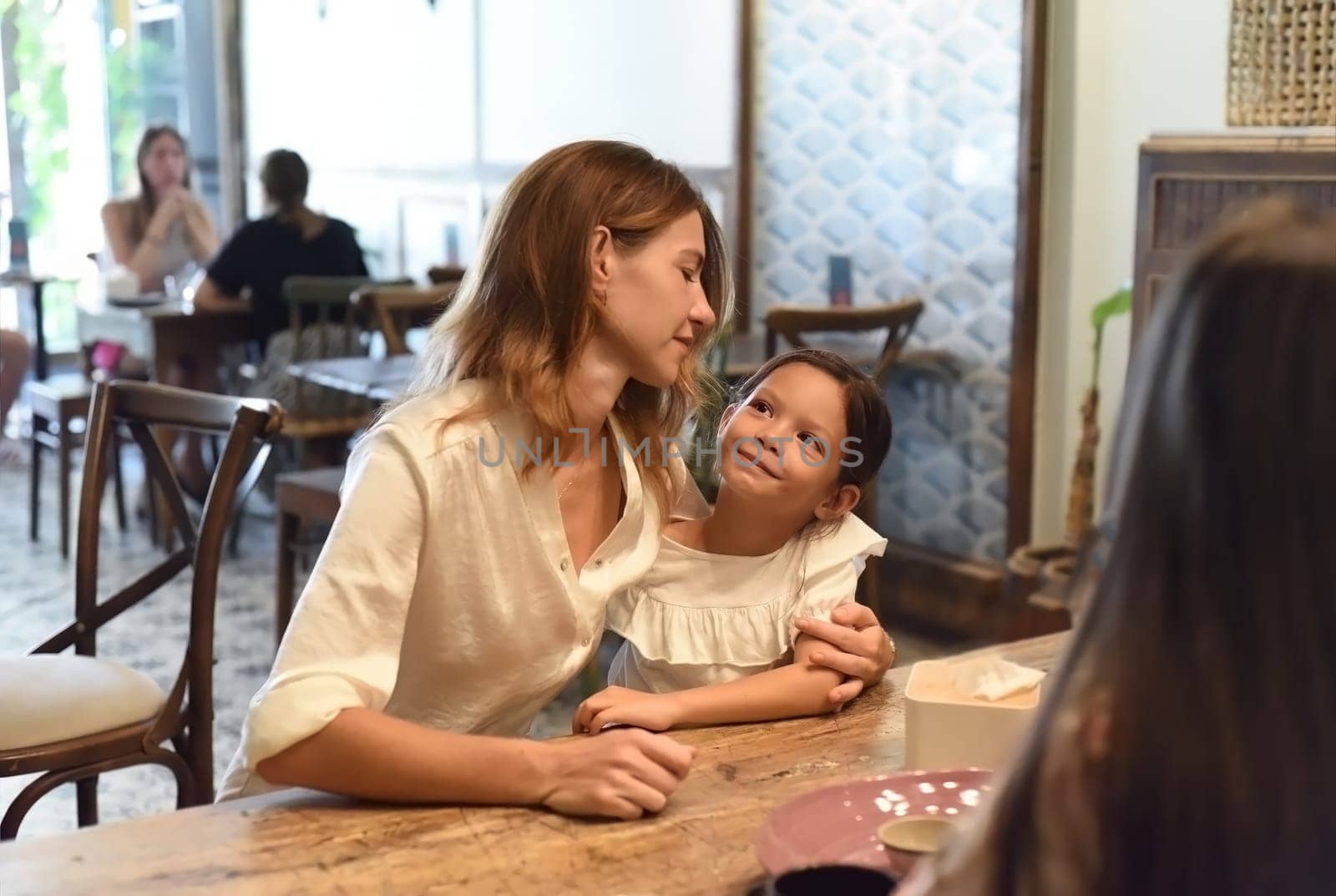 Little girl and her mother hugging and looking at each other in a cafe