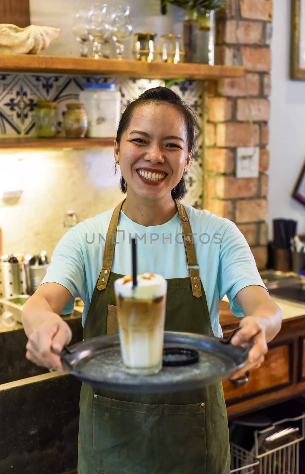 Vietnamese waitress holding glass of ice latte coffee on a tray in cafe