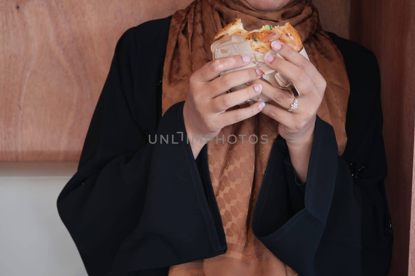 A woman clad in traditional clothing enjoys a hearty sandwich indoors.