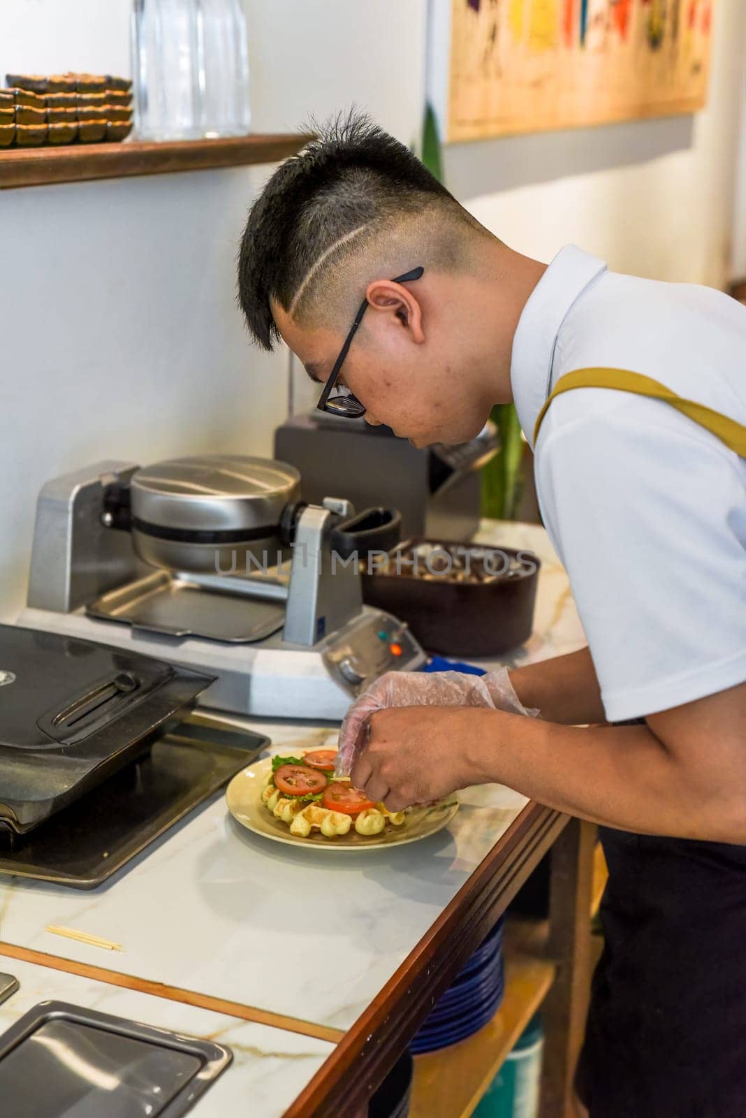Vietnamese man chef serving fresh belgian waffles with chicken, cheese and tomato on the plate