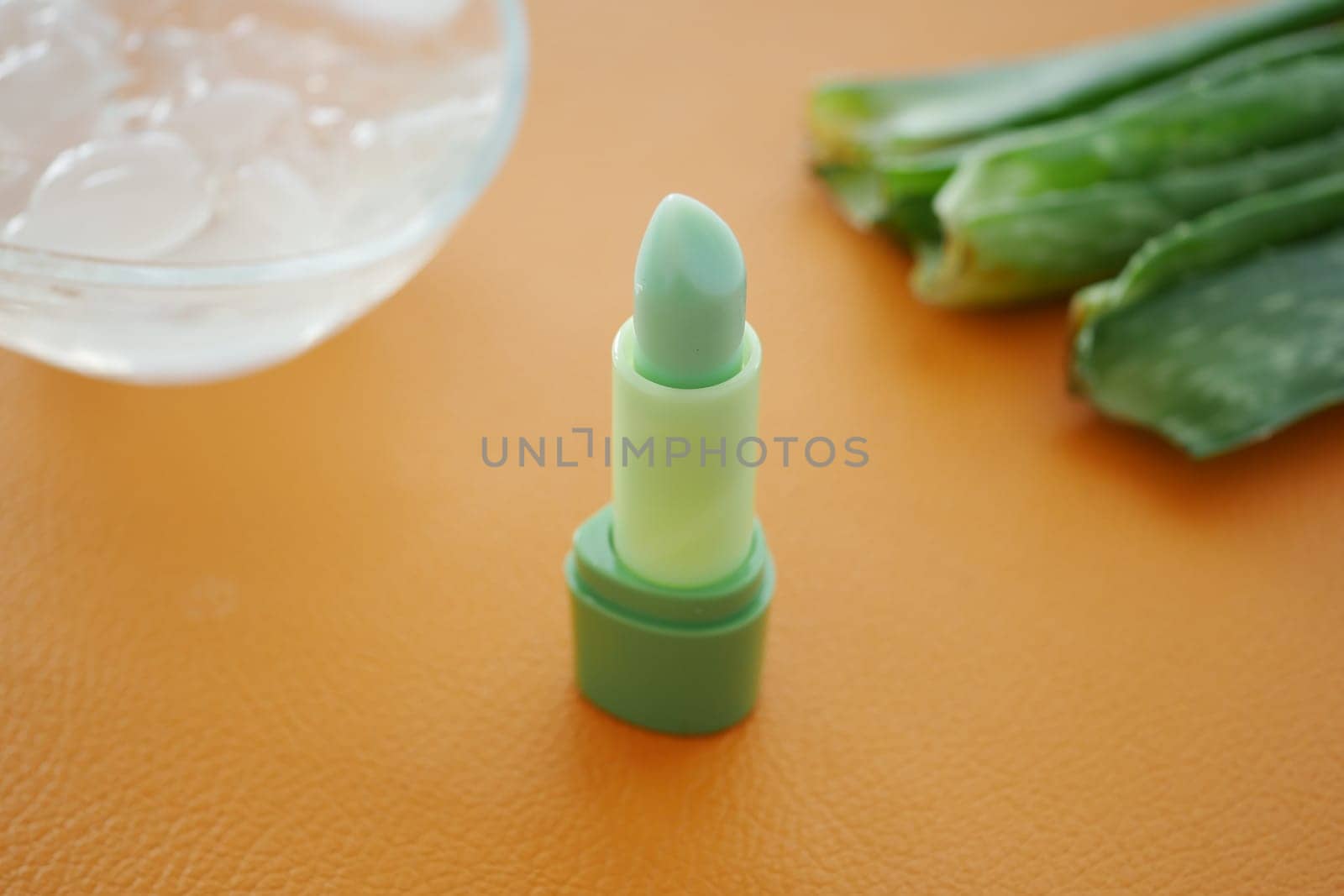 Fresh green lip balm beside aloe vera leaves and ice cubes.