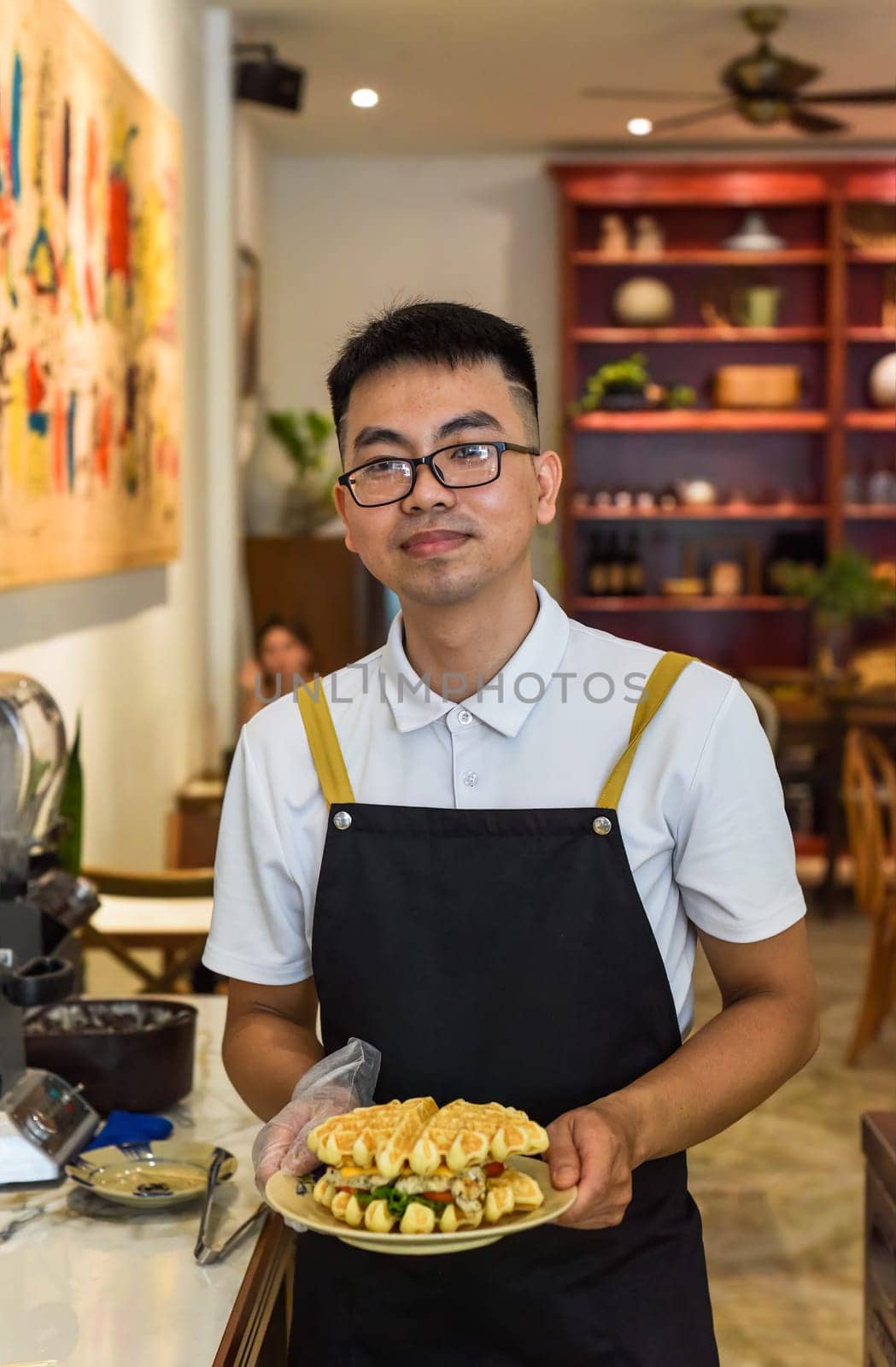 Vietnamese man chef in uniform holding fresh baked belgian waffles with chicken, cheese and vegetables