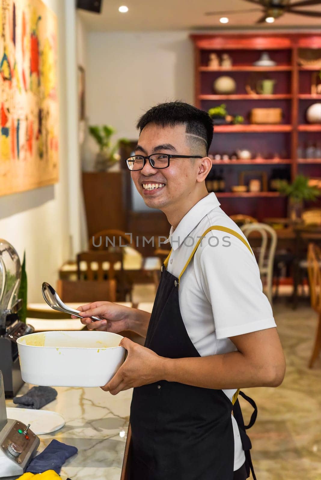 Vietnamese man chef in uniform holding spoon and bowl with liquid dough for belgian waffles