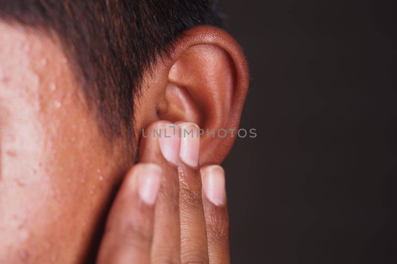 A person is gently holding their ear with fingers, focused and attentive.