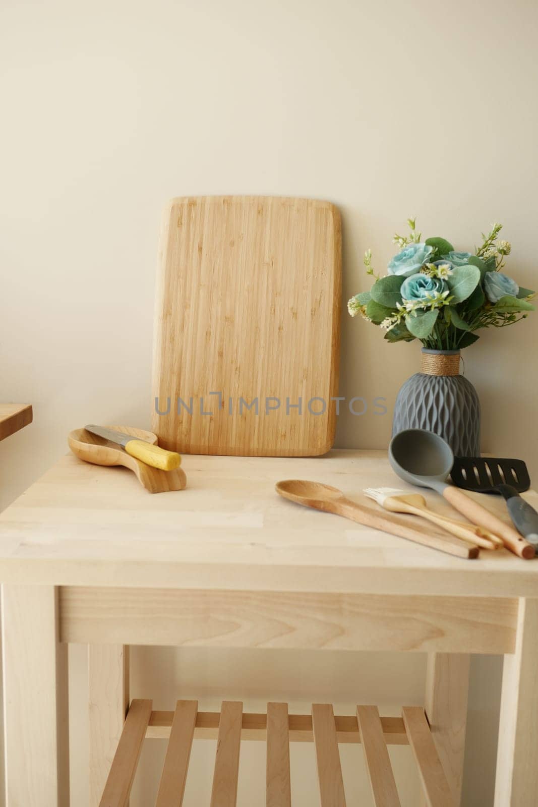 A tidy kitchen counter with a wooden board, utensils, and flowers.