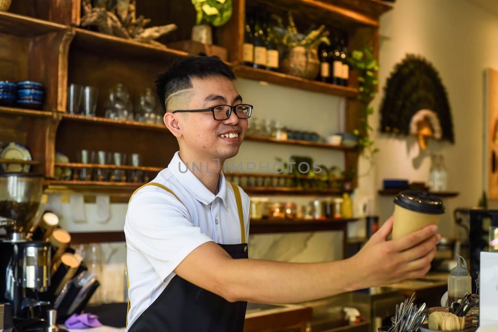 Vietnamese smiling waiter holding paper cups with coffee in a cafe