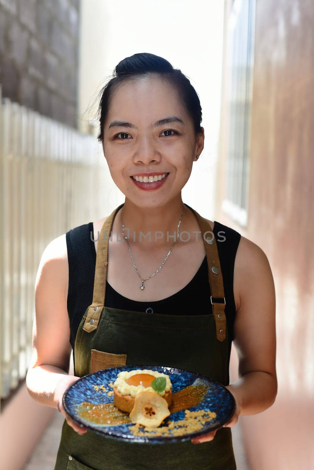 Vietnamese woman waitress in apron holding apple tart on a blue plate