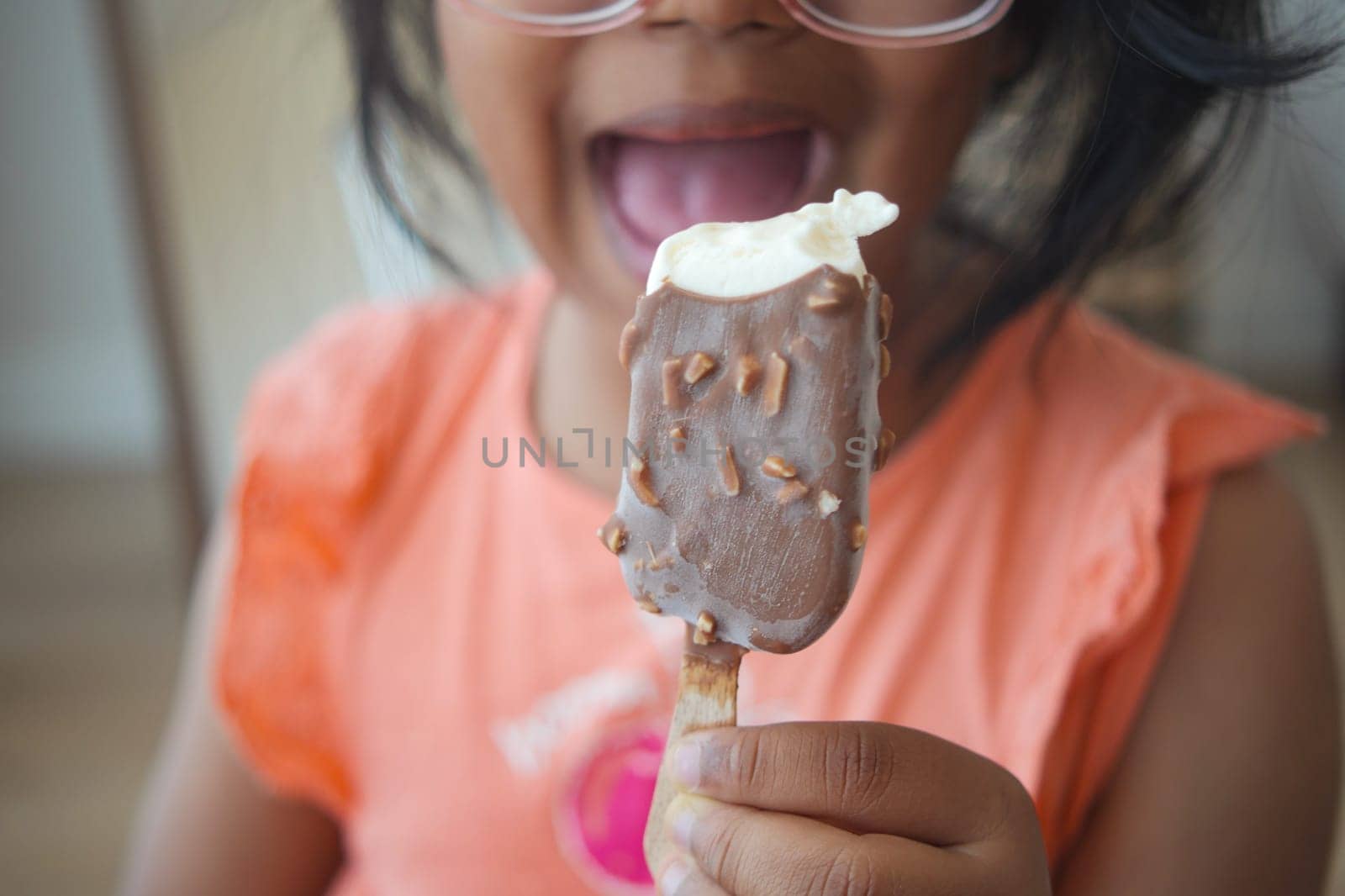 Young girl with glasses happily holds chocolate ice cream treat, smiling wide.