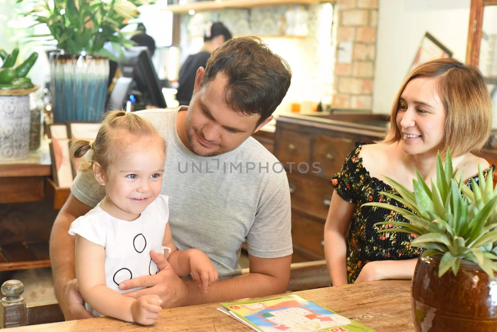 Young parents look at their daughter and smile together in cafe