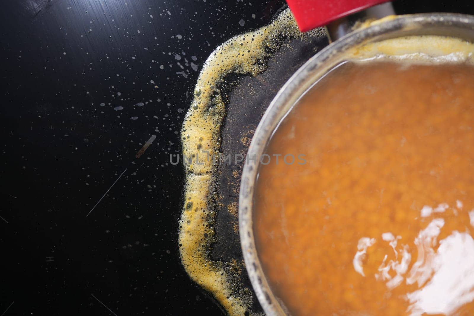 Closeup of burnt oil bubbling in a pan, leaving residue buildup on the stoves surface
