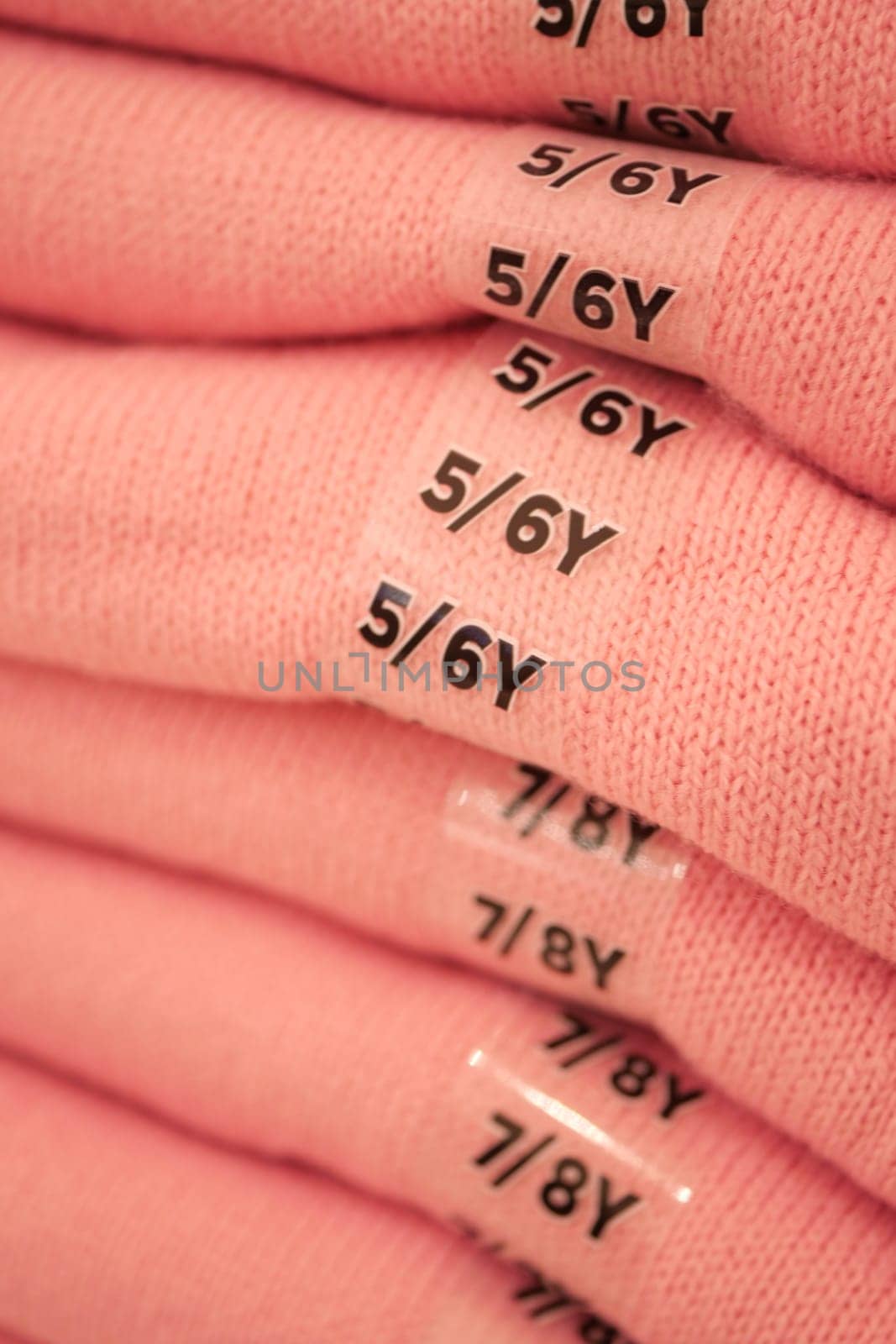 Stacked pink garments display size labels for young children.