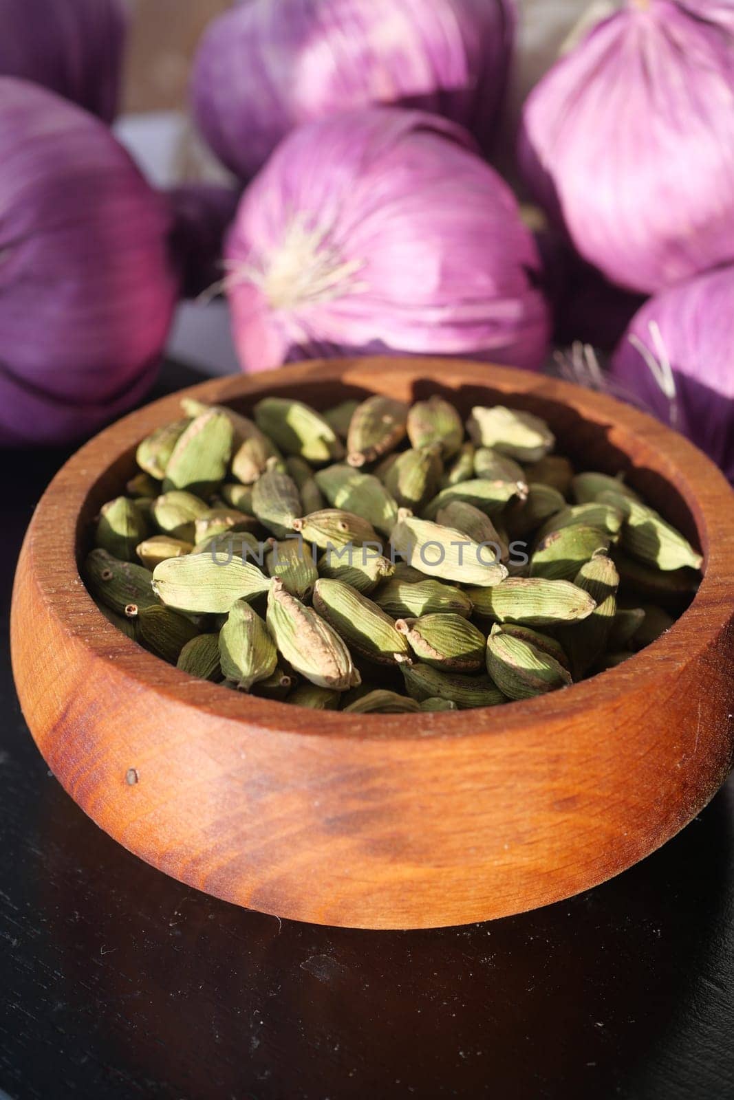 Cardamom seeds fill a bowl, surrounded by purple onions.