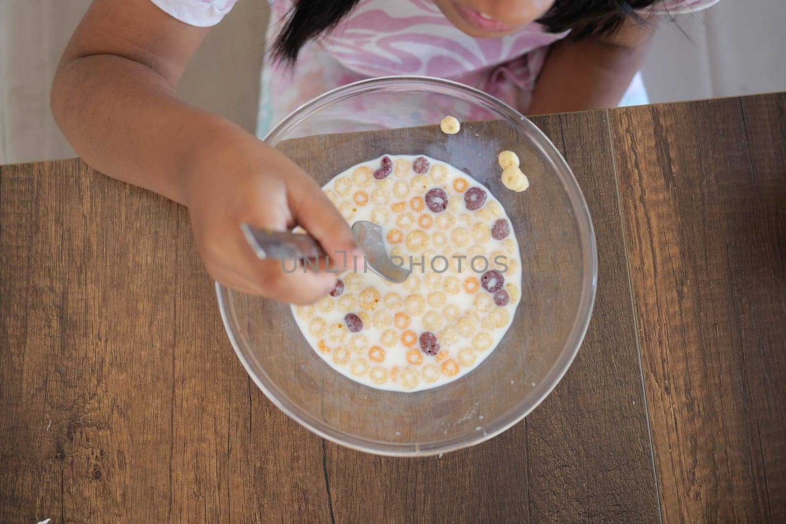 A young child is happily eating cereal with milk in a bowl.