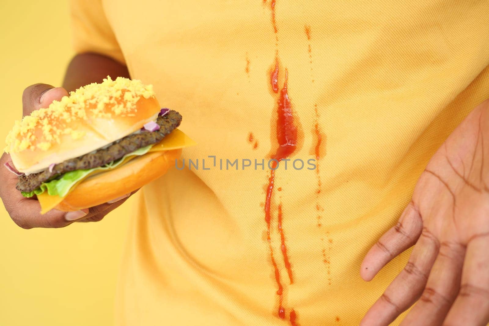 A person spills ketchup on their shirt while holding a burger.