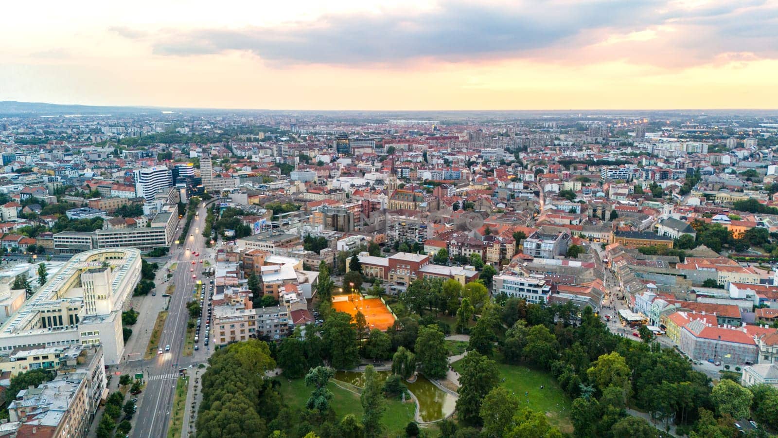 Aerial view of Novi Sad Serbia cityscape with green park streets and vibrant buildings at sunset