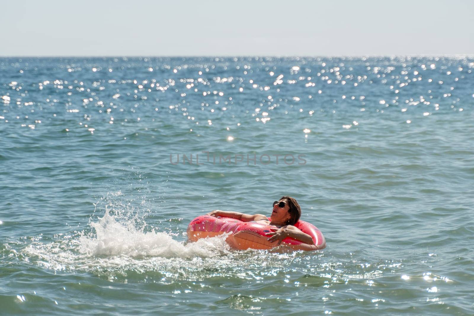 A person floats on a pink inflatable ring in the ocean, the water is sparkling with sunlight.