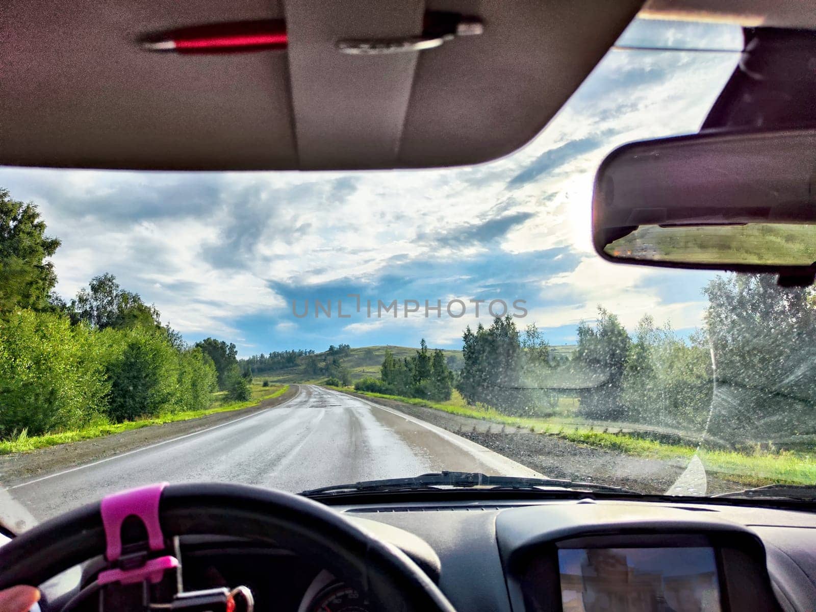 view through car windshield of nature landscape with green field, mountains, white clouds. Hand of woman on steering wheel. Female traveler