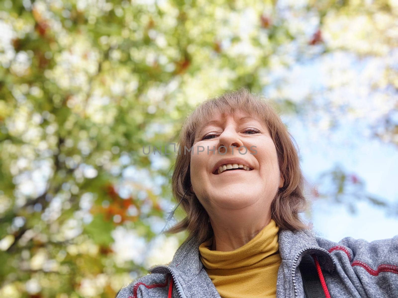 Middle-aged woman takes a cheerful selfie during her nature trip, surrounded by vibrant autumn leaves and blue skies