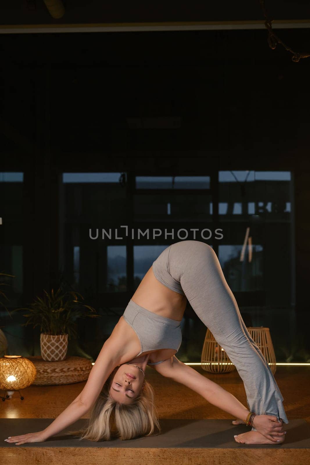 In a tranquil indoor setting, a woman engages in the downward-facing dog pose during her yoga routine. The warm glow from decorative lighting creates a peaceful atmosphere as she focuses on her practice in the early evening.