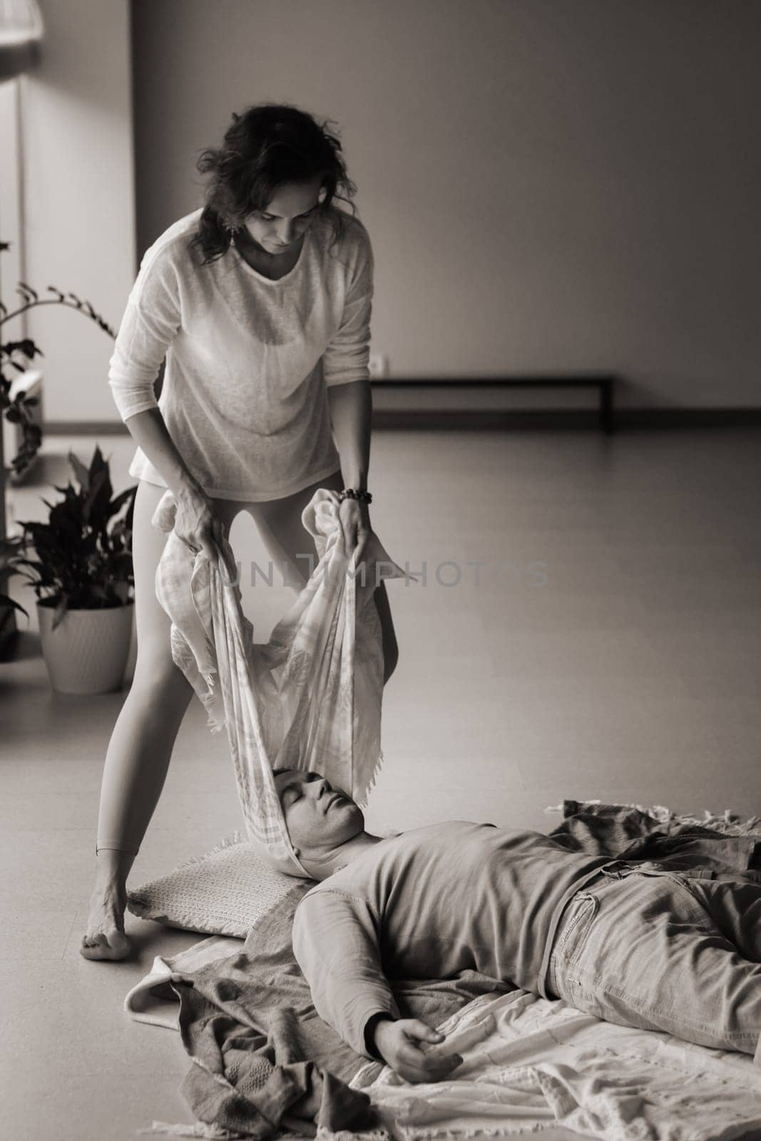 A therapist gently drapes a colorful scarf over a patient lying on a comfortable mat in a calm studio. The serene space is adorned with plants, creating a peaceful environment for healing and relaxation.