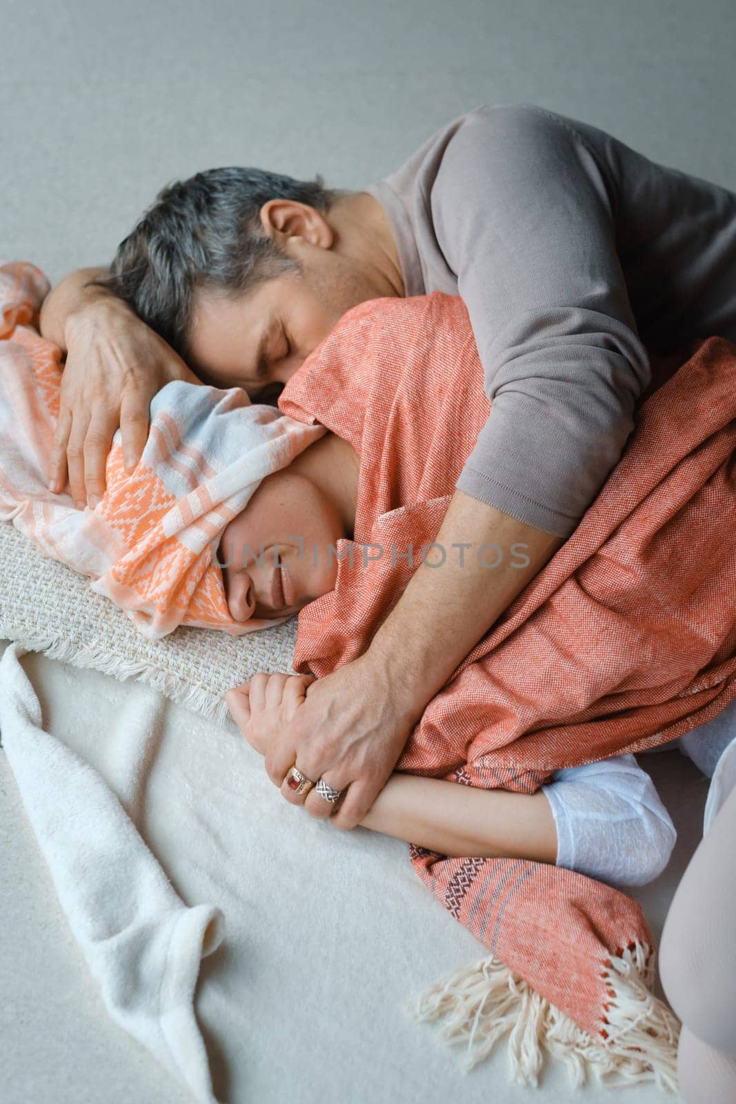 Two individuals share a tender embrace on a soft floor, wrapped in warm blankets. The gentle touch and closeness suggest a deep connection and comfort in each other s presence during a peaceful afternoon at home.