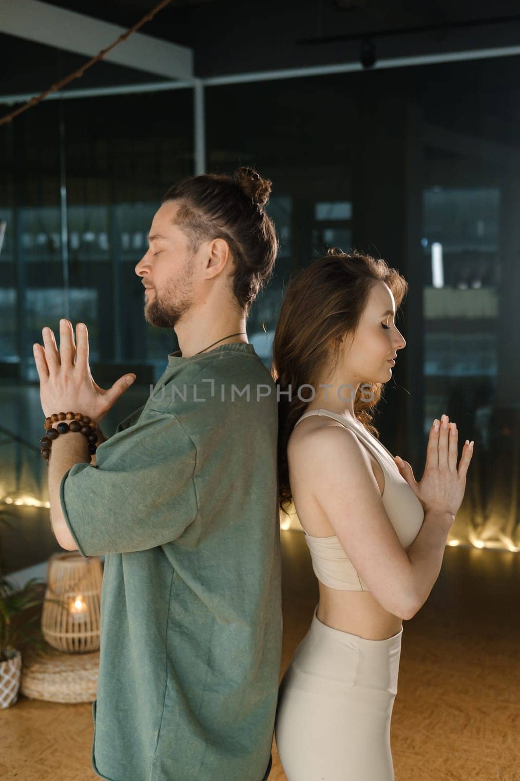 Two practitioners engage in a meditative exercise, seated back to back in a tranquil indoor environment. The soft lighting creates a calming atmosphere, enhancing their focus on breathing and mindfulness during the session.
