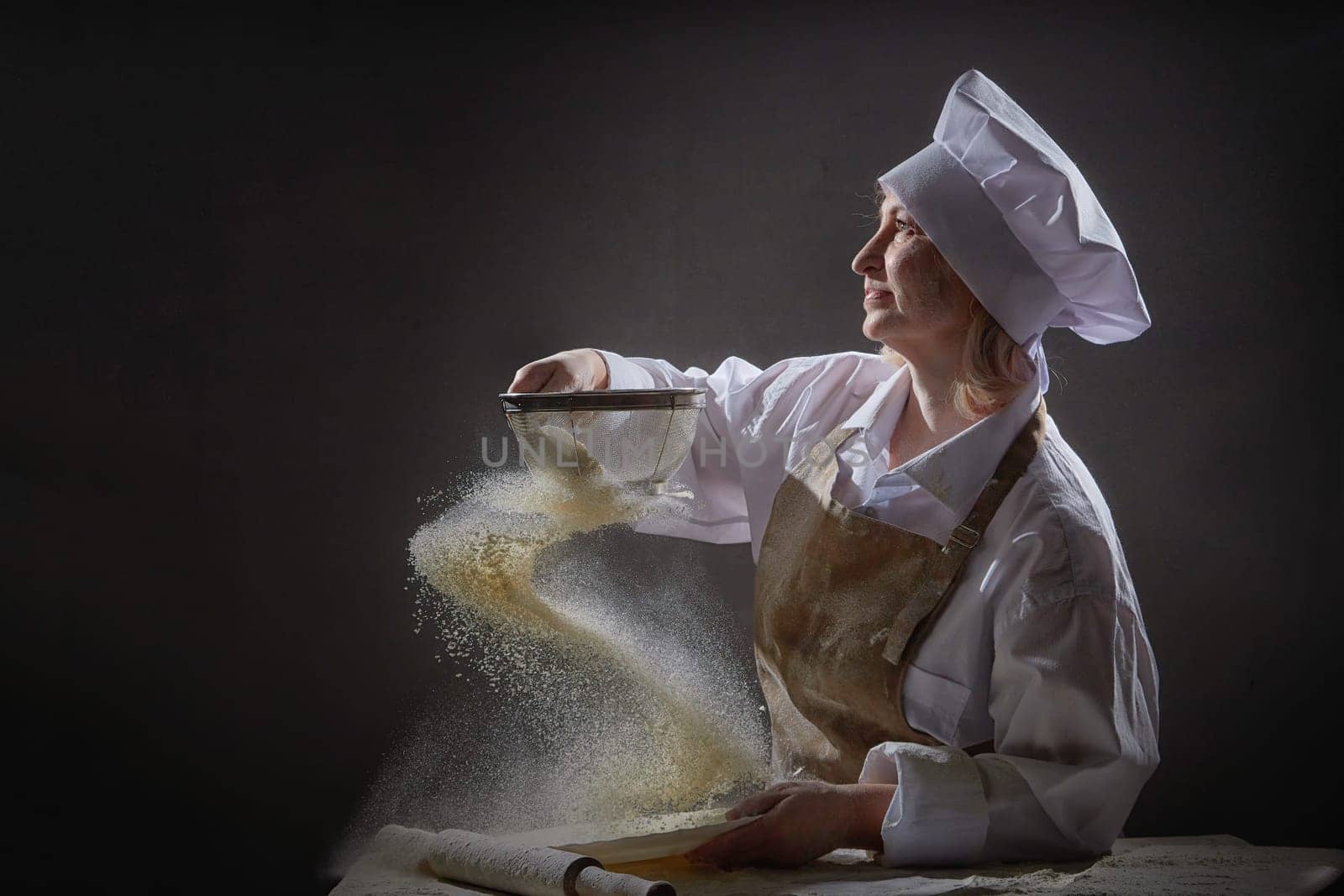 An elderly woman sifts flour with joy and creativity while engaging in a humorous kitchen photo shoot, showcasing her culinary skills.
